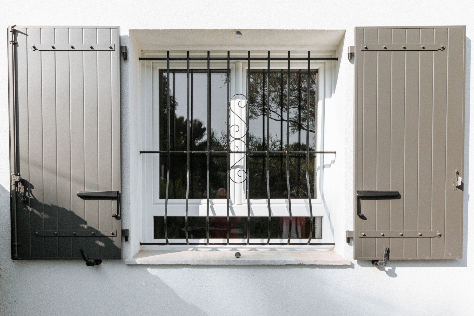 Fenêtre avec deux volets battants de couleur taupe ouvert.