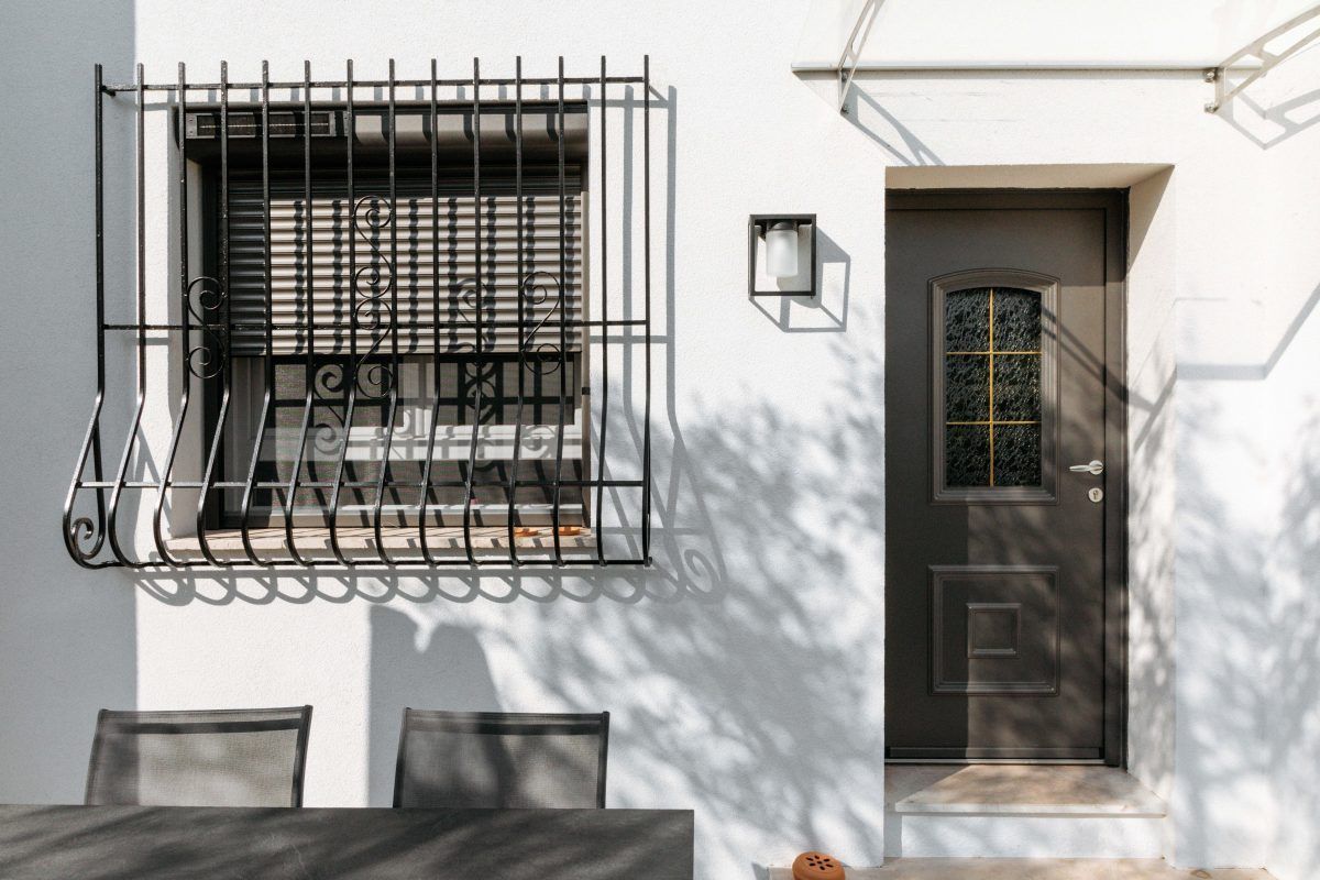 Façade d'une maison blanche avec une fenêtre derrière une grille et une porte d'entrée vitrée grise