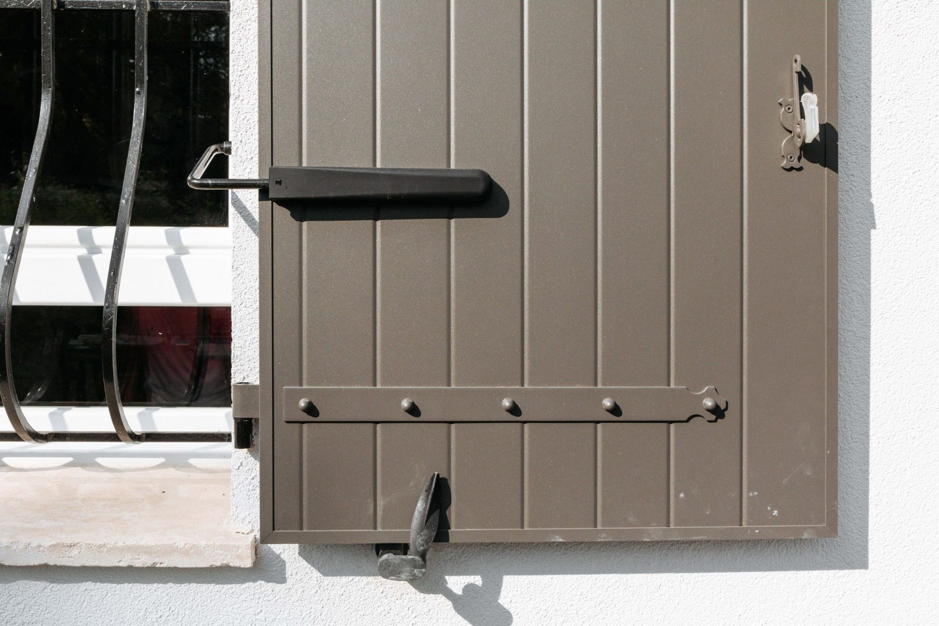 Gros plan sur un volet battant couleur taupe ouvert et attaché.