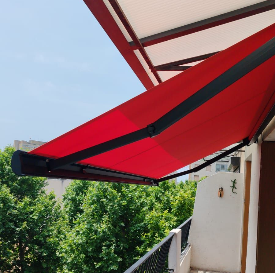 Un store banne rouge rétractable est déployé sur un balcon, offrant de l'ombre.