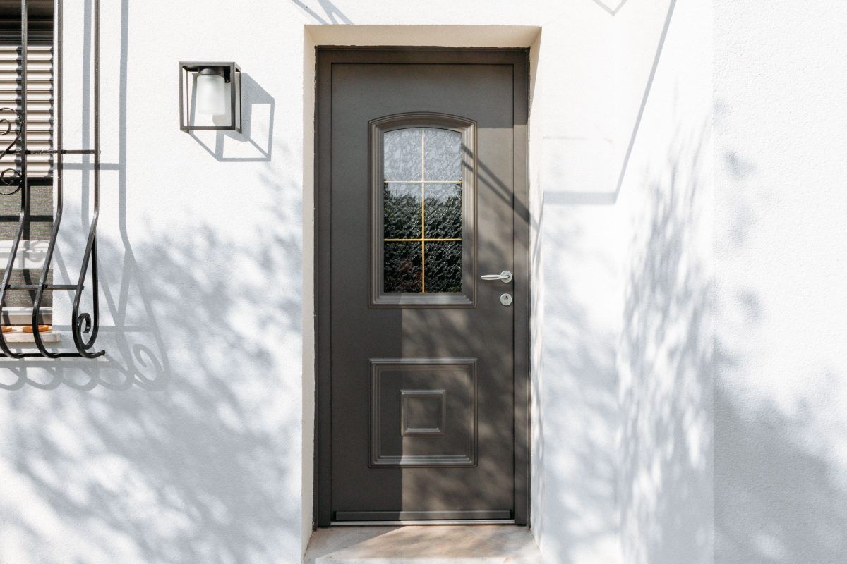 Porte d'entrée vitrée de couleur grise sur un mur de maison crépis de couleur blanche.
