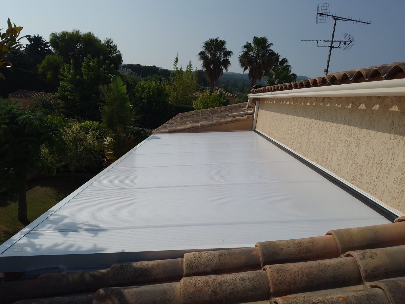 Auvent blanc installé sur un toit de tuiles, avec des arbres et le ciel en arrière-plan.
