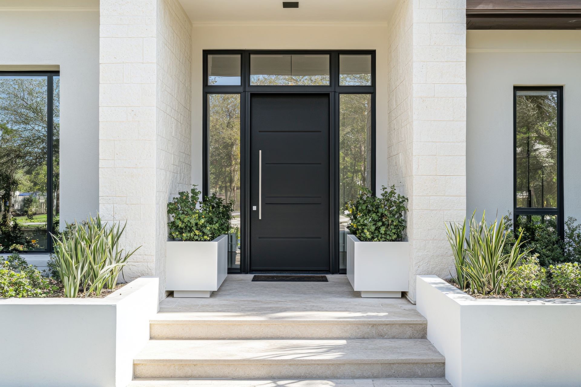 Devant de maison avec une porte d'entrée encadrée par des fenêtres, avec plusieurs bacs à fleurs.
