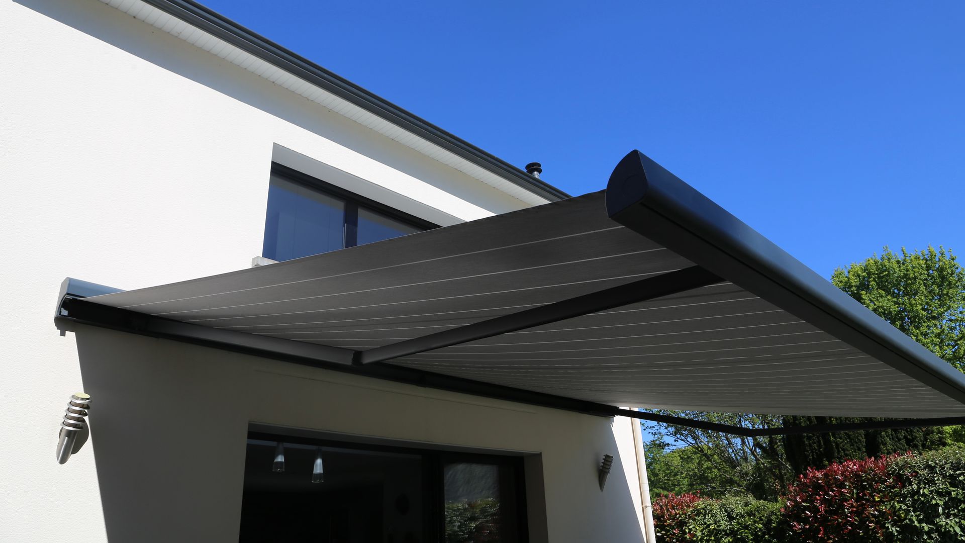 Gros plan d'un store rétractable fixé sur le côté d'un bâtiment moderne de couleur claire.
