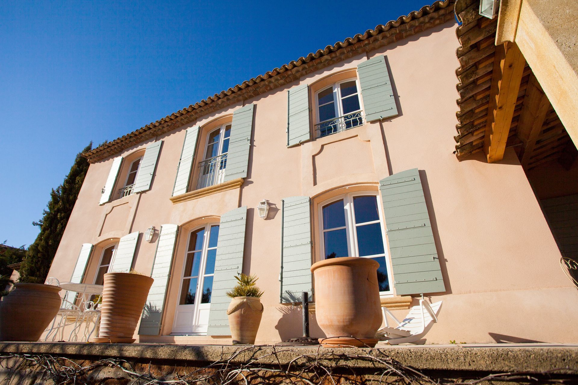 Façade de maison avec des fenêtres grises et volets de couleur vert pastel avec un sommet arrondi