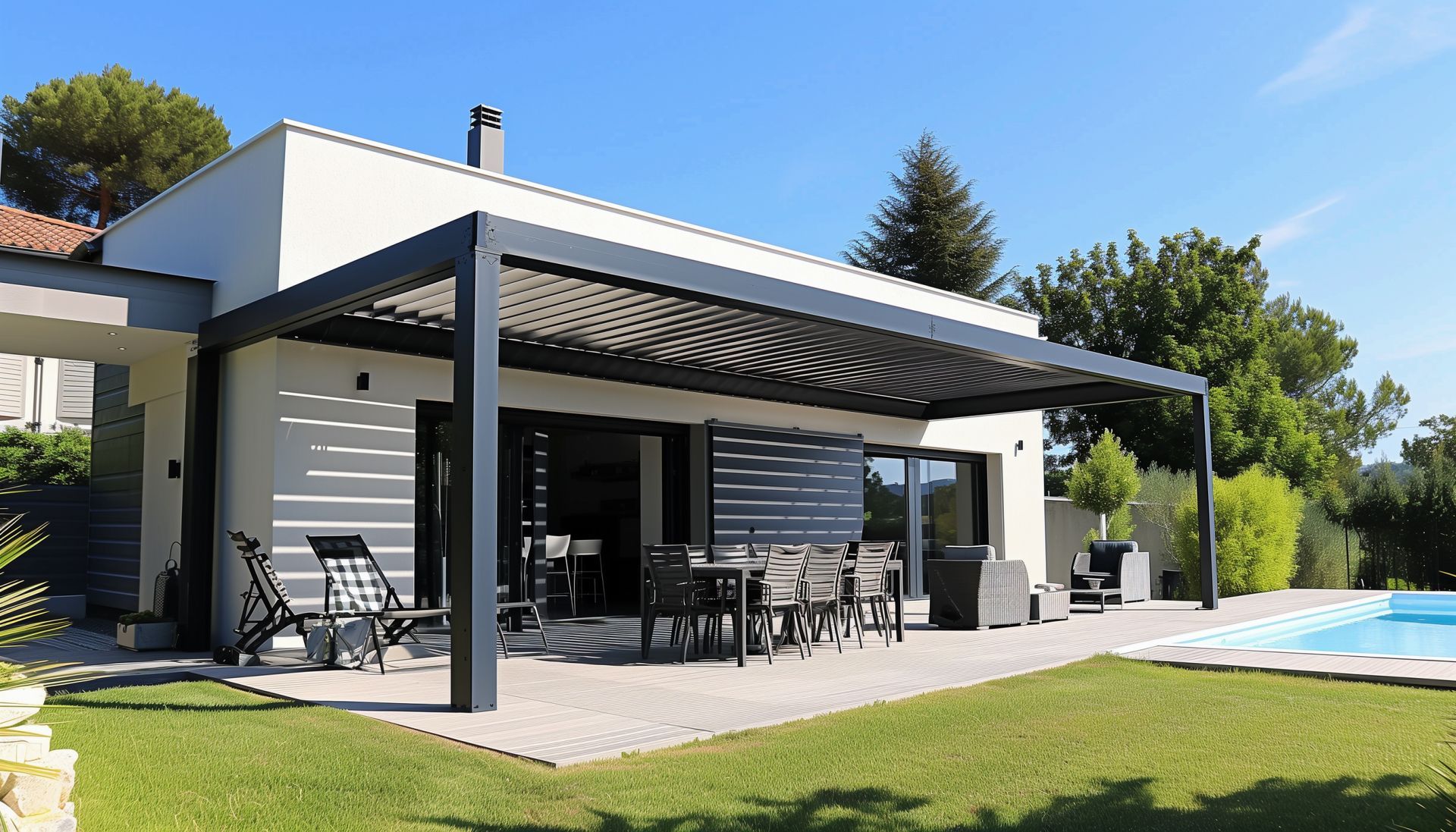 Maison moderne avec une pergola gris foncé au-dessus d'une terrasse. On aperçoit des chaises, une table et une piscine.