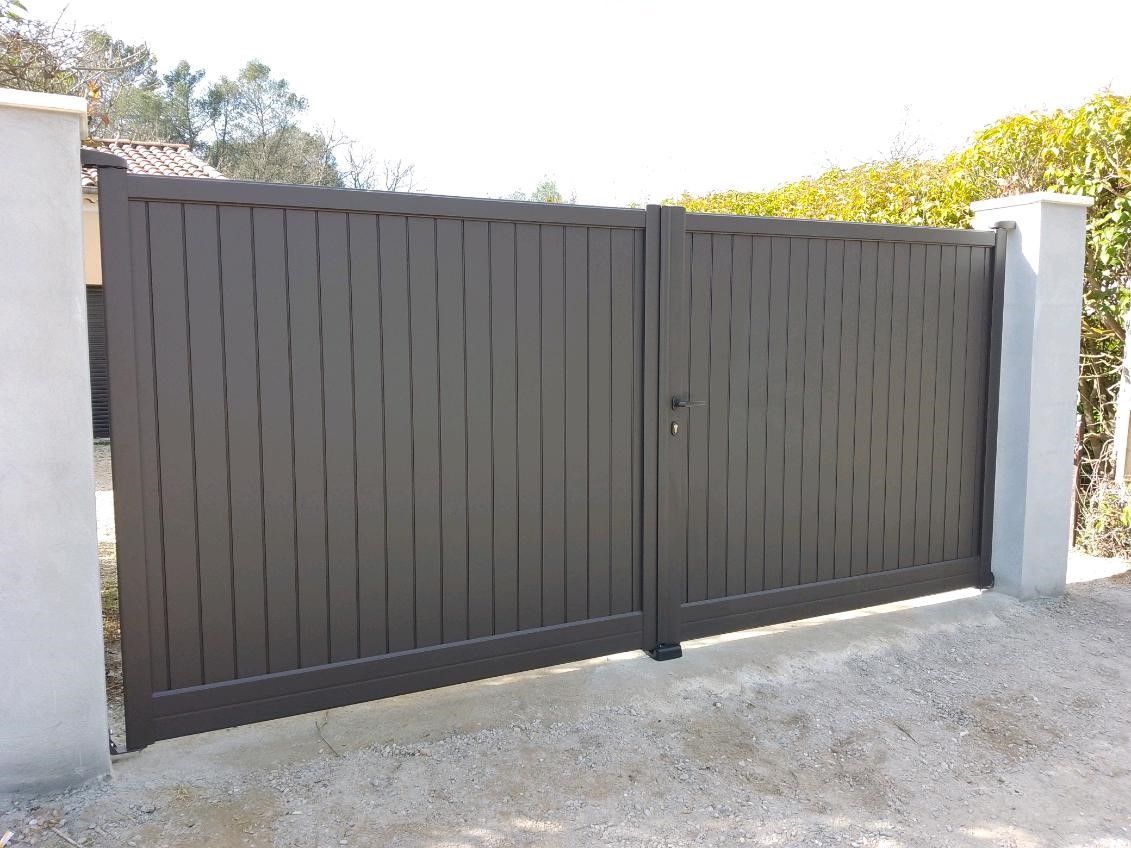 Portail à deux battants, non ajourés avec deux piliers blancs, on y aperçoit une haie à l'arrière.