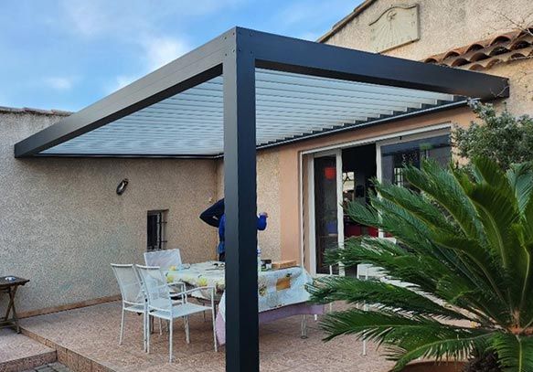 Une pergola avec un palmier au premier plan. Elle met en valeur un aménagement extérieur alliant architecture et aménagement paysager, créant un espace ombragé propice à la détente.