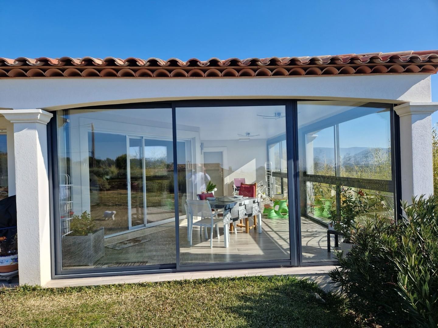 Grandes baies vitrées entourant une terrasse avec une table et des chaises