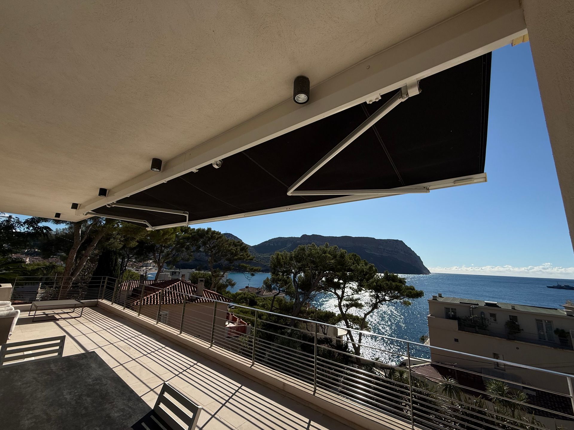 Balcon avec store noir, donnant sur l'océan et un ciel bleu.