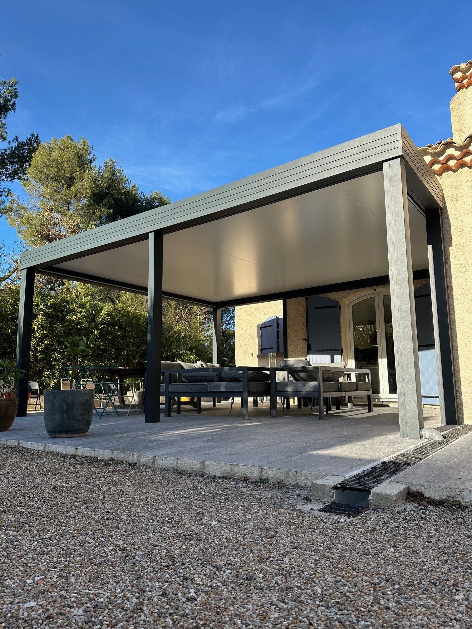 Pergola moderne en aluminium gris sur une terrasse avec du mobilier d'extérieur assorti