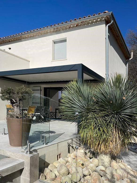 Une maison avec un patio orné de plantes variées. L'espace extérieur met en valeur la beauté de la nature et les éléments architecturaux du bâtiment.
