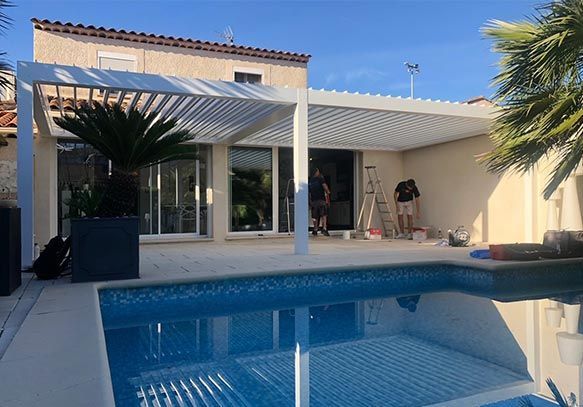 Une piscine située devant une maison avec une grande pergola blanche, mettant en valeur un espace extérieur conçu pour la détente et les loisirs.
