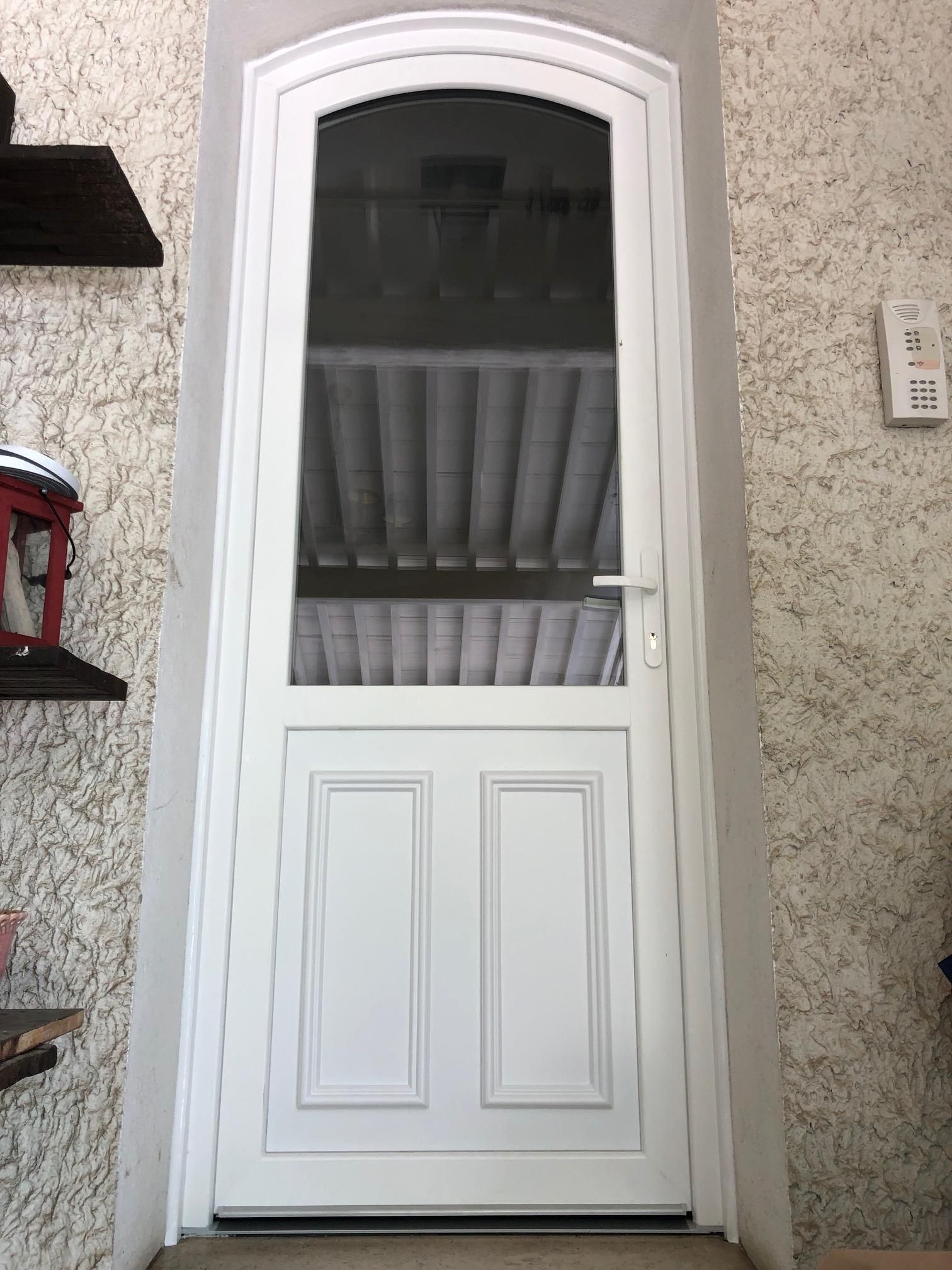 Porte d'entrée vitrée en pvc blanc d'une maison avec une façade avec un crépis en relief.