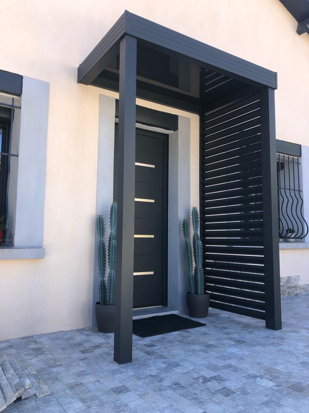 Une porte noire encadrée d'un cadre noir assorti, agrémentée d'une jardinière noire à proximité. Ce décor évoque une esthétique élégante et moderne, typique de l'architecture contemporaine. La photo s'inscrit dans le contexte du bâtiment et de l'immobilier, mettant en valeur des éléments de décoration extérieure.