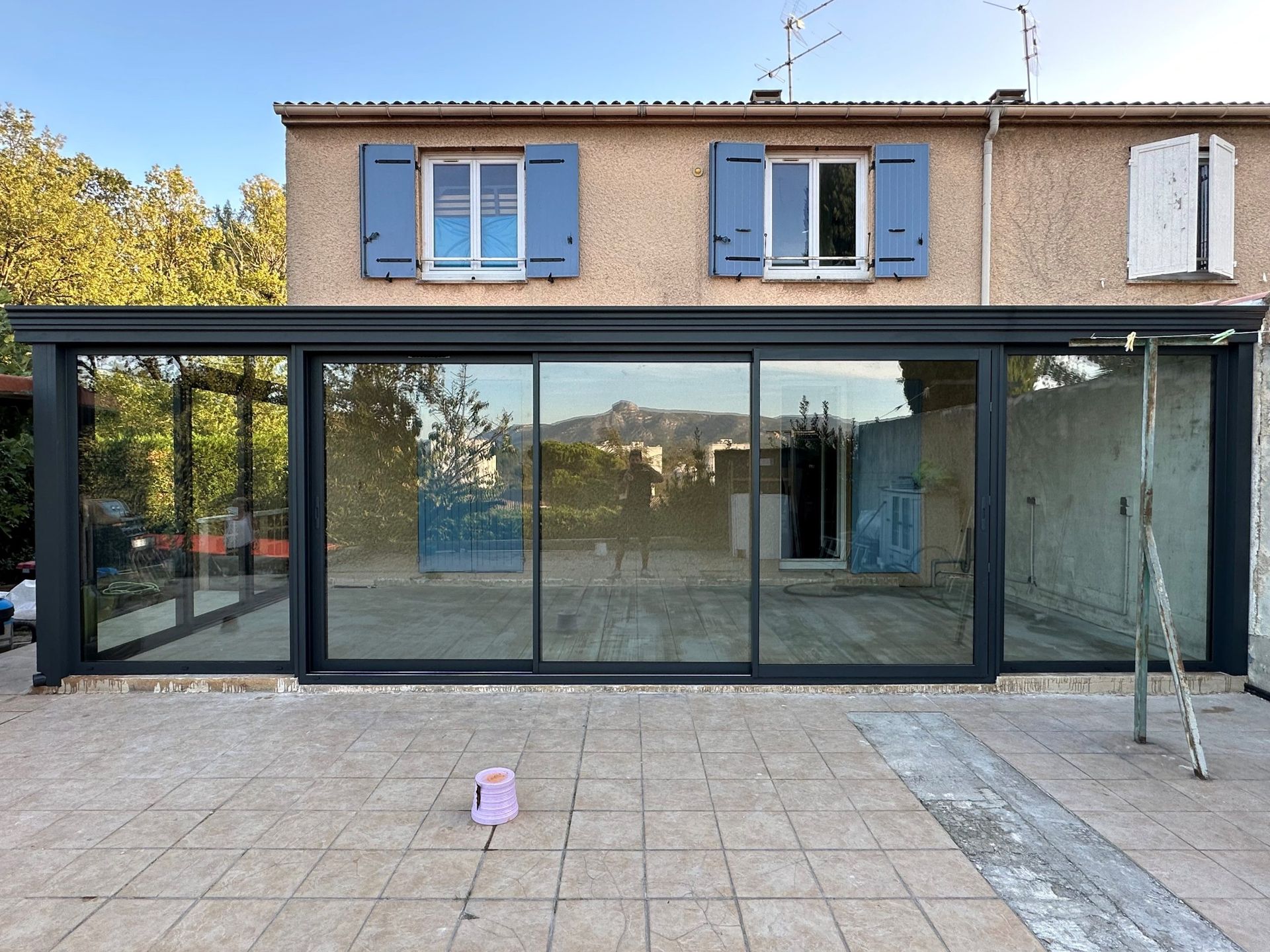 Grande véranda avec un vitrage anti effraction devant une maison avec des fenêtres aux volets bleus