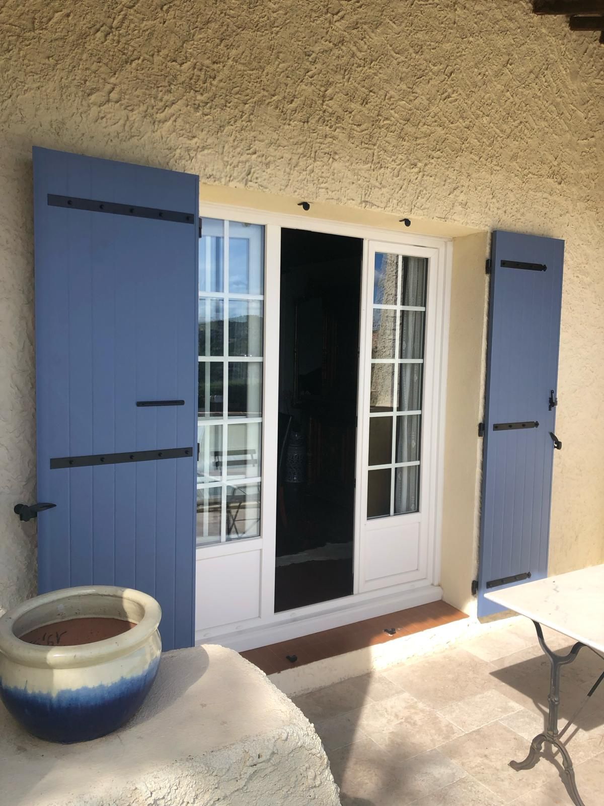 Porte fenêtre ouverte avec des volets battants bleus ouverts