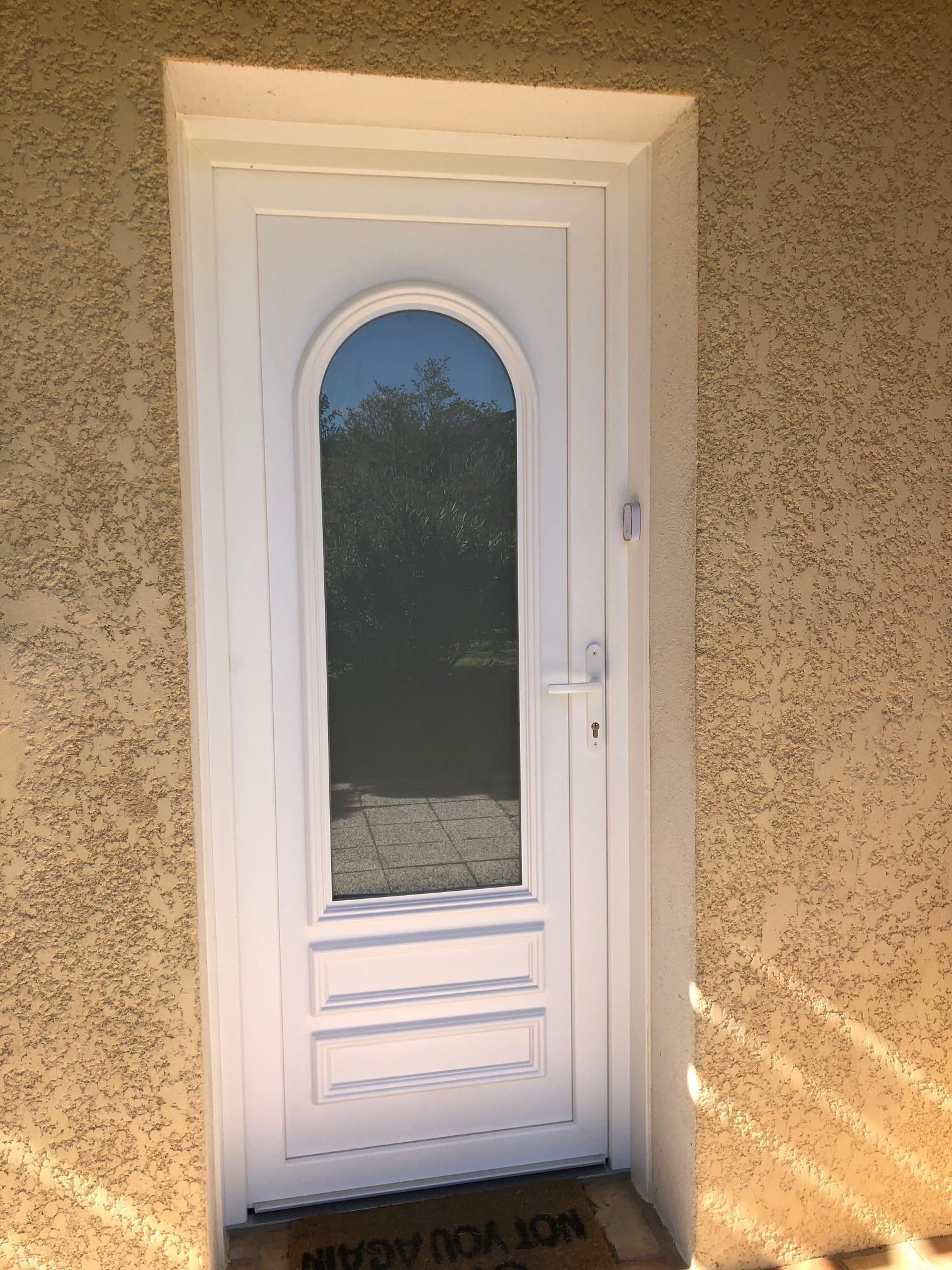 Porte d'entrée vitrée en pvc blanc d'une maison avec une façade jaune.