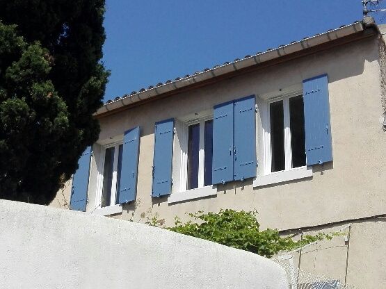 Étage d'une maison avec 3 fenêtre aux volets battants bleus ouverts.