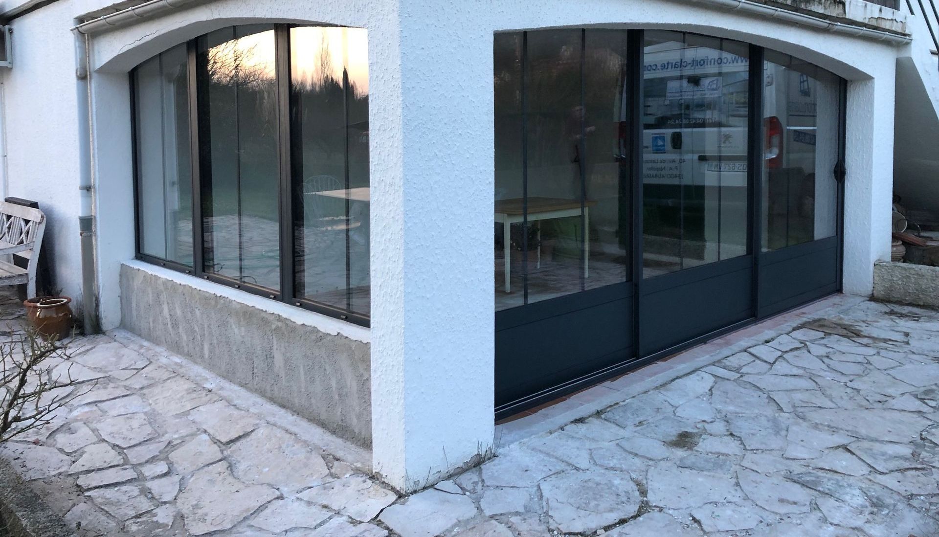 Un bâtiment caractérisé par ses baies vitrées, soulignant une architecture moderne. Il est situé en extérieur, entouré d'un trottoir menant à son entrée.