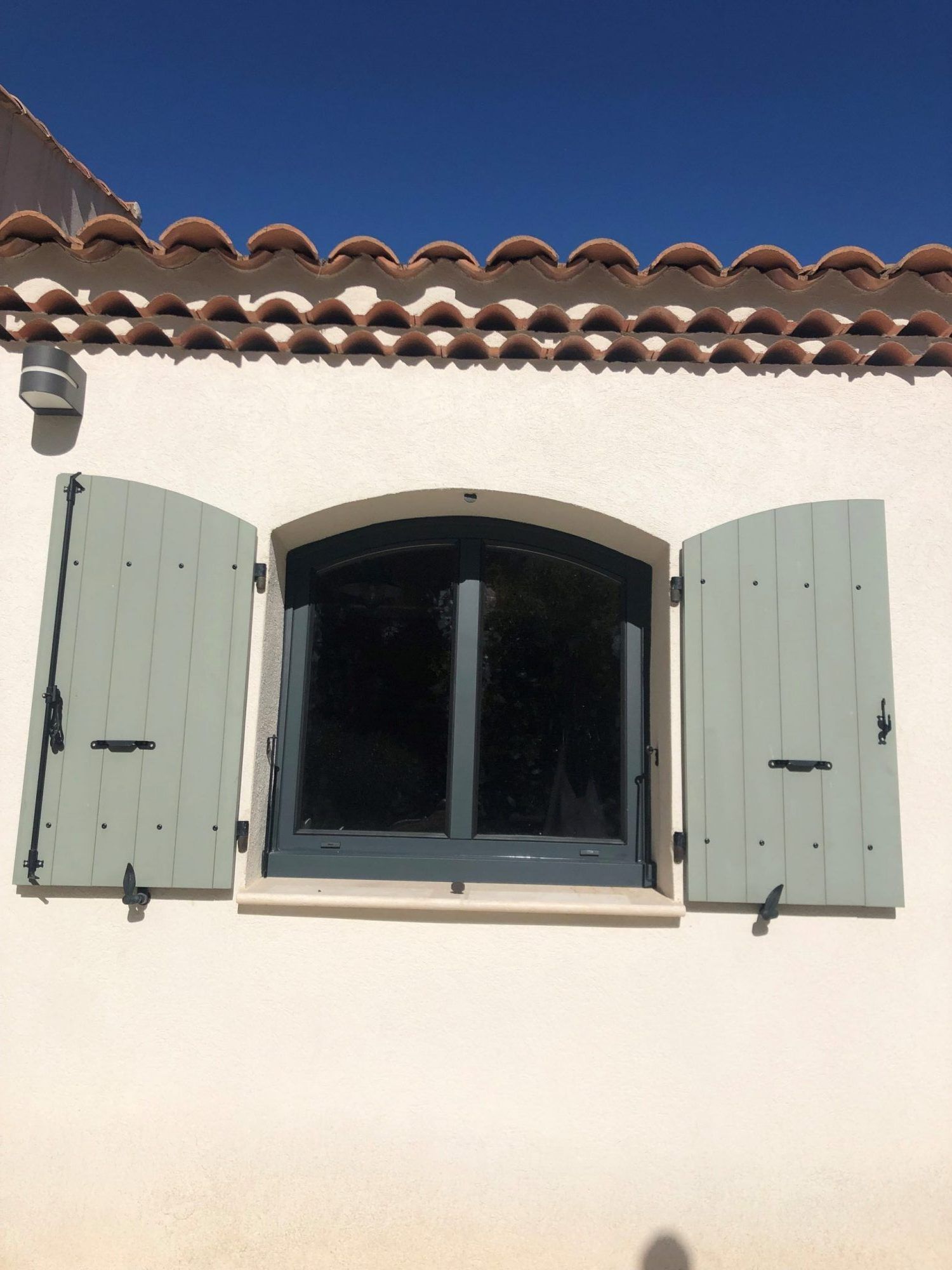 Fenêtre grise et volets de couleur vert pastel avec un sommet arrondi