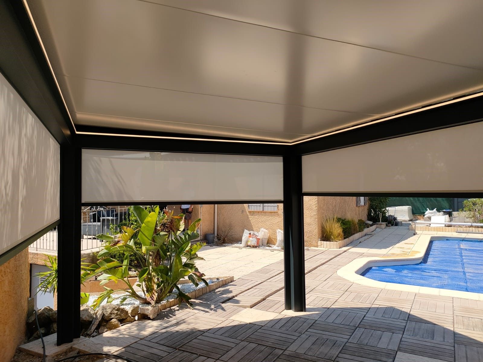 Une pergola avec vue sur une piscine et un bâtiment adjacent. Le décor suggère une ambiance de vie en plein air, alliant loisirs et design.