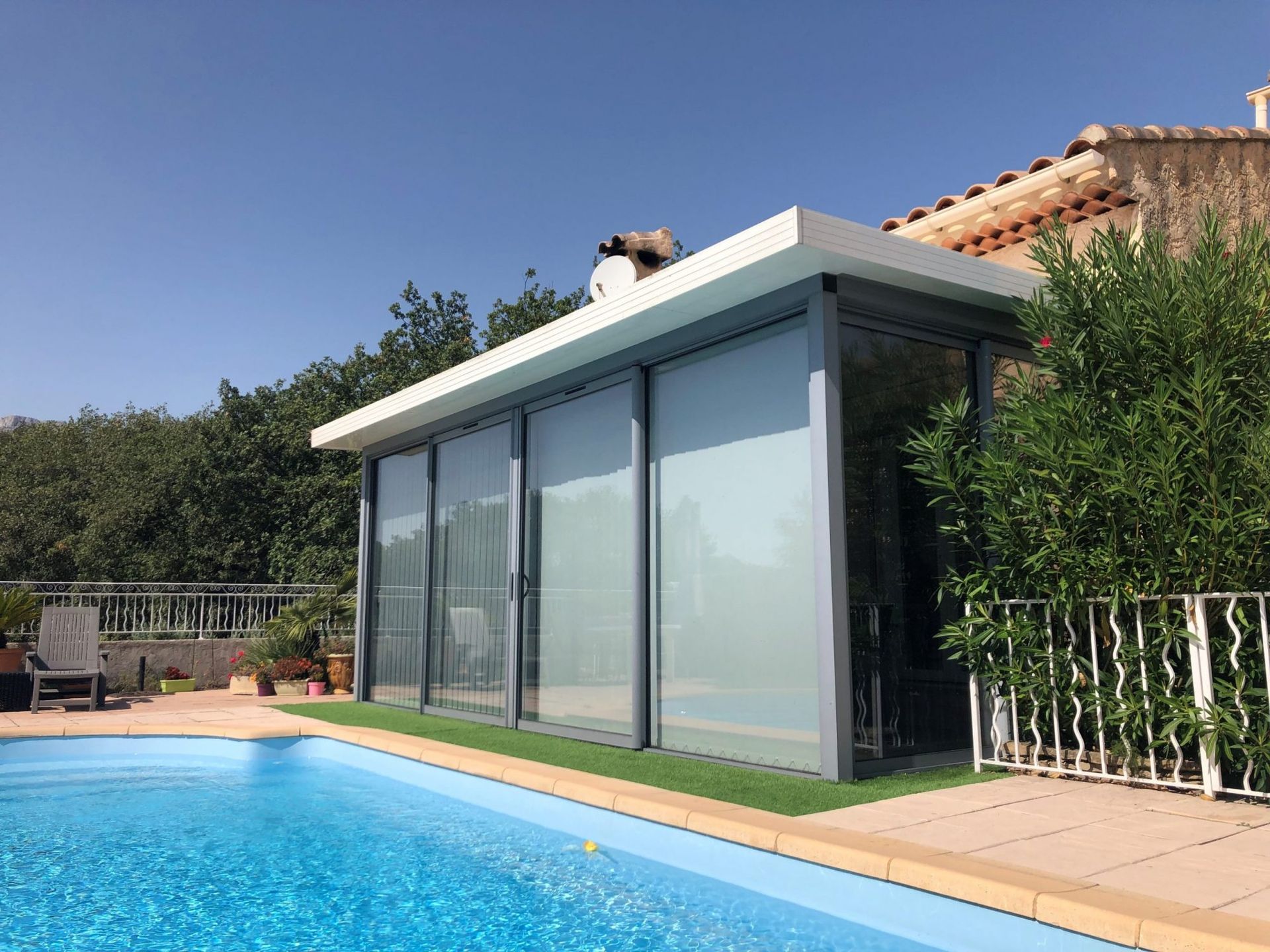 Une piscine adjacente à une véranda. Le décor intègre des éléments extérieurs tels que les arbres et le ciel, soulignant le design architectural de la propriété.