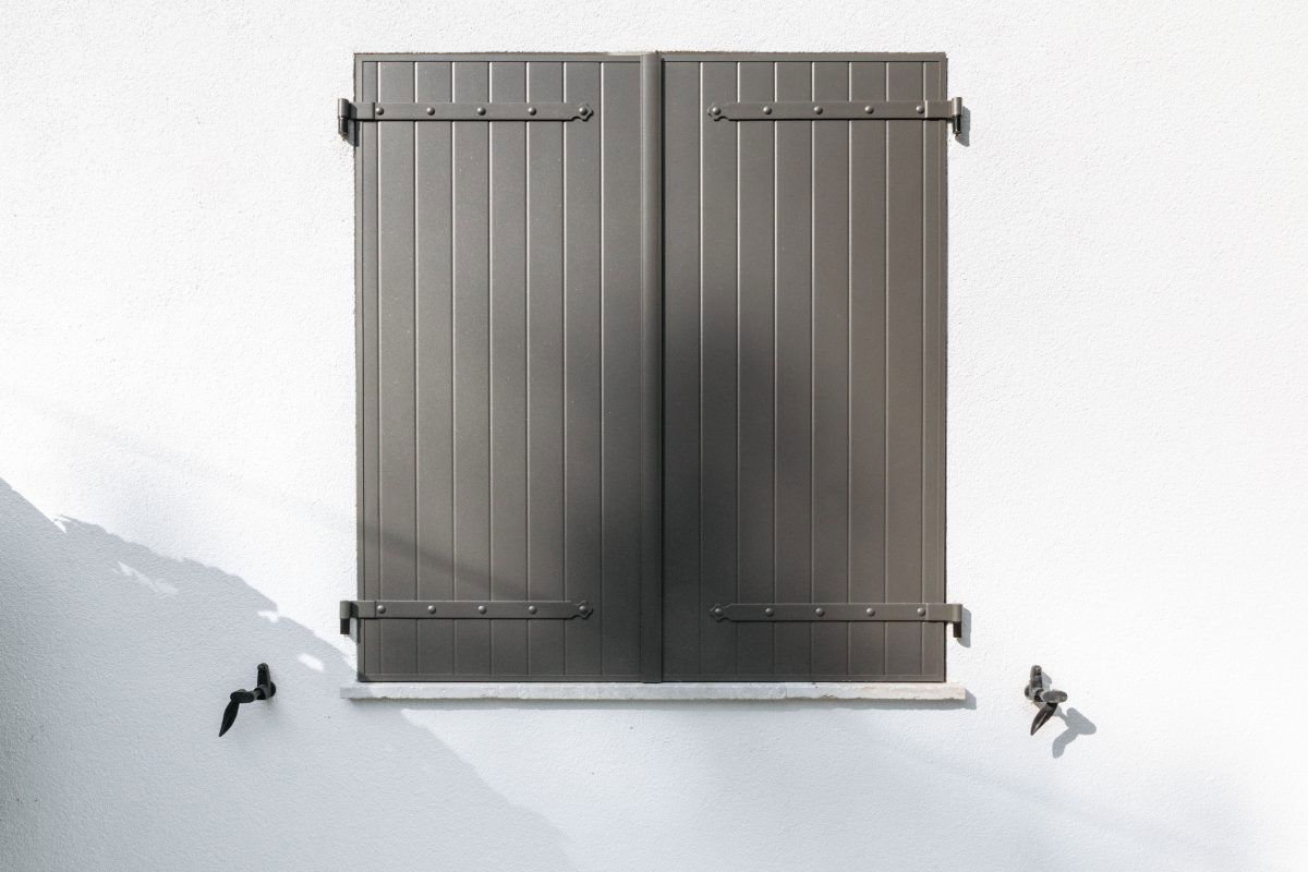 Volets battant gris fermé sur une façade de maison blanche