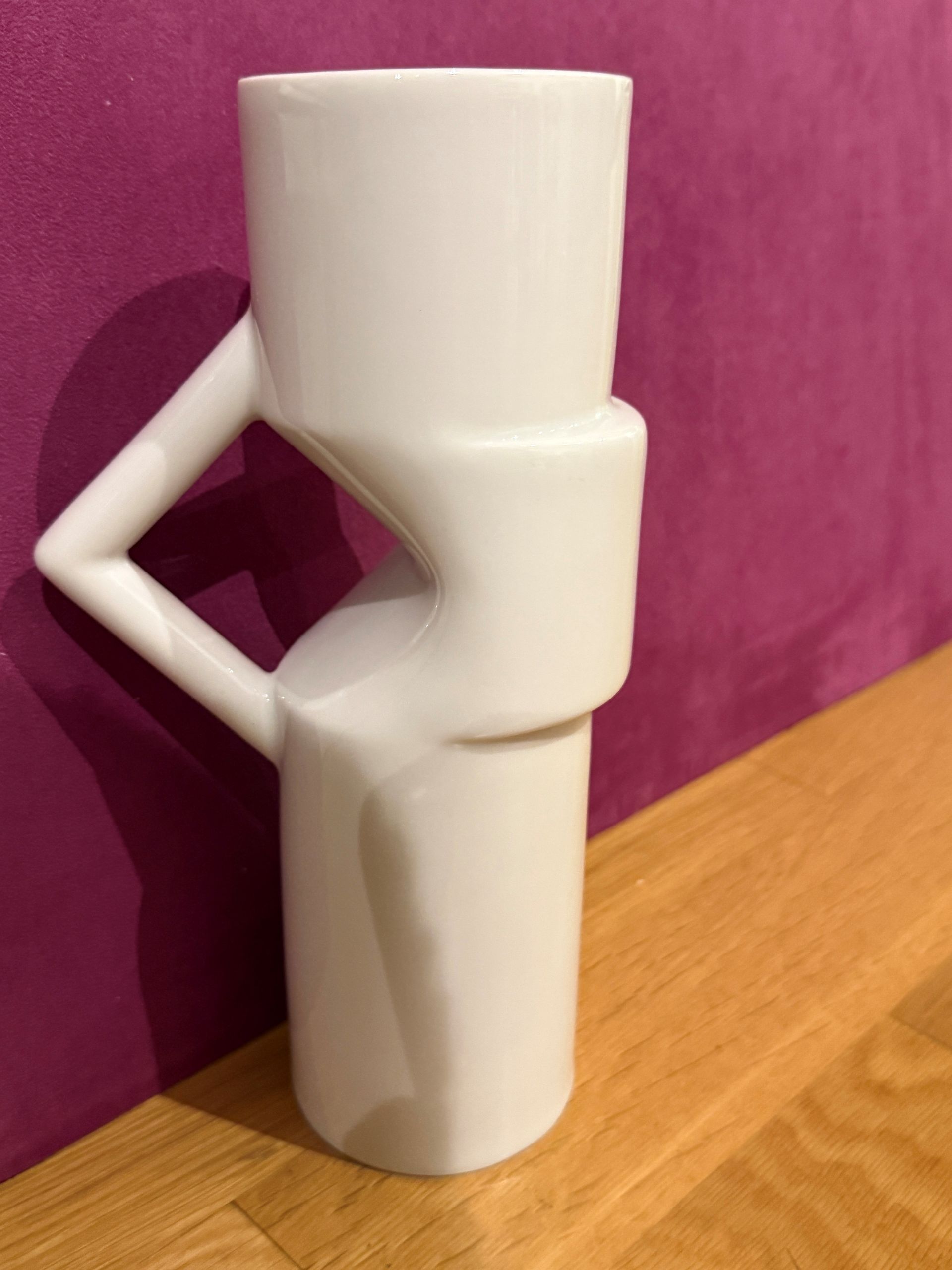 Weiße Keramikvase mit geometrischem Muster auf Holzboden vor violetter Wand.