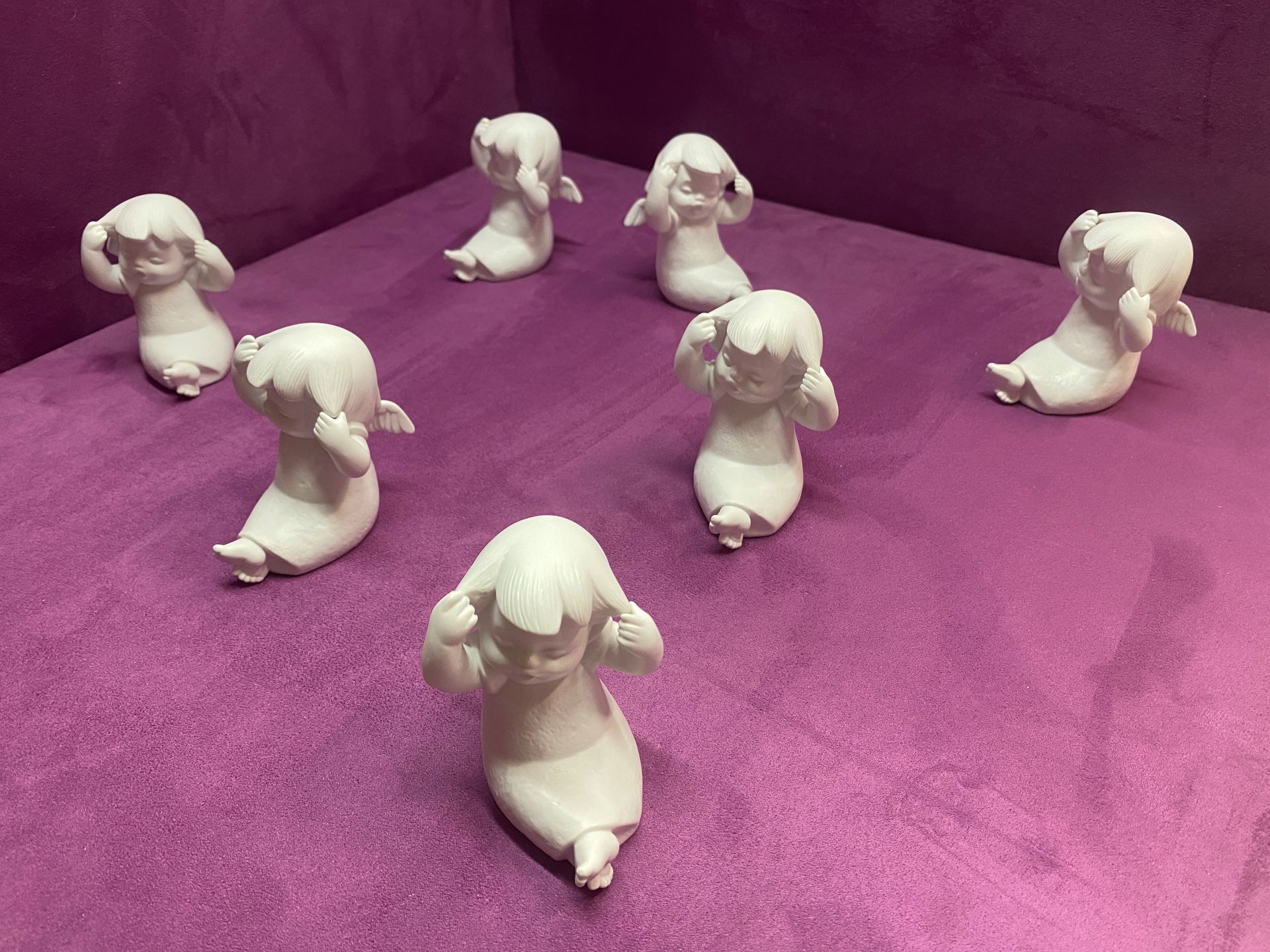 Acht weiße Figuren sitzender Gestalten, die sich die Ohren zuhalten, auf violettem Grund.