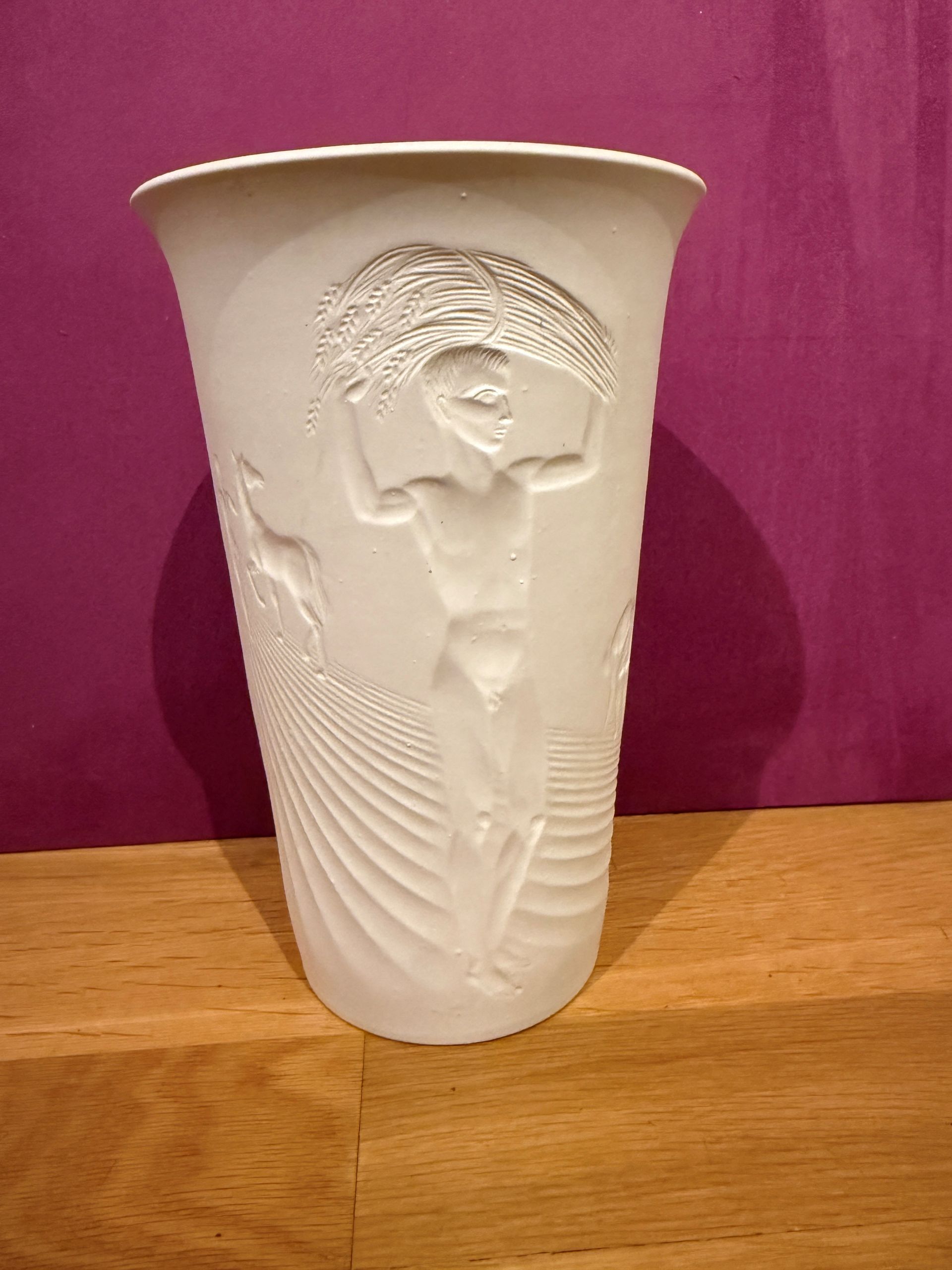 Weiße Keramikvase mit erhabenem Relief einer Person, die ein Bündel trägt, umgeben von anderen strukturierten Bildern.