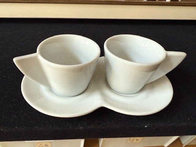 Zwei weiße Espressotassen mit Untertassen, auf einer dunklen Oberfläche.