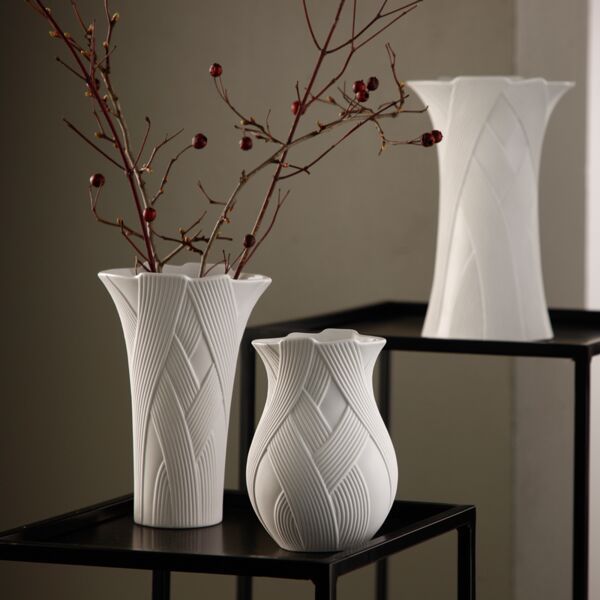Drei weiße Keramikvasen mit strukturierten Mustern, eine davon mit Zweigen, an denen rote Beeren hängen.