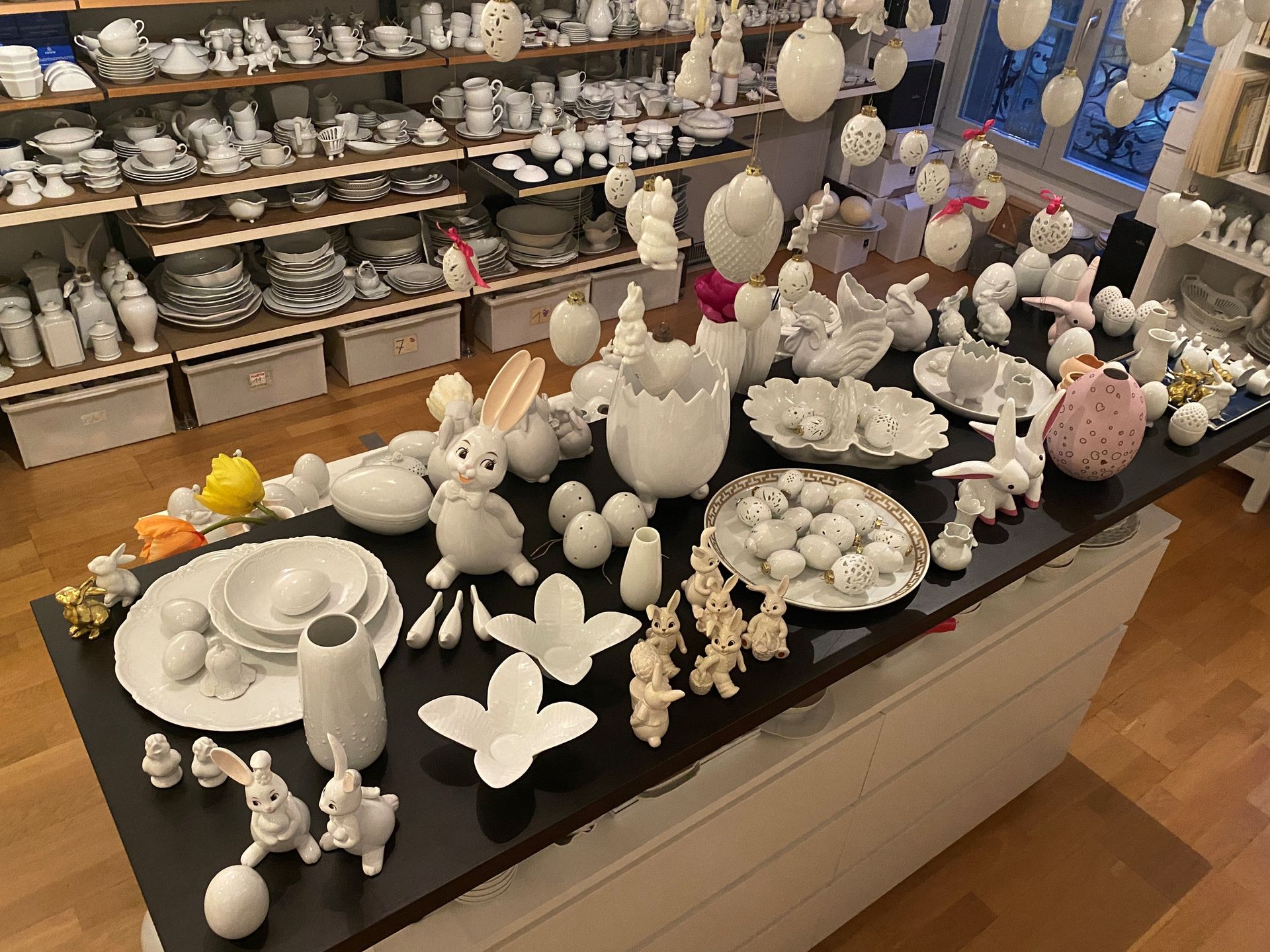 Osterdekoration mit Keramikhasen, Eiern und Geschirr auf einer schwarzen Theke, im Hintergrund Regale mit ähnlichen Artikeln.