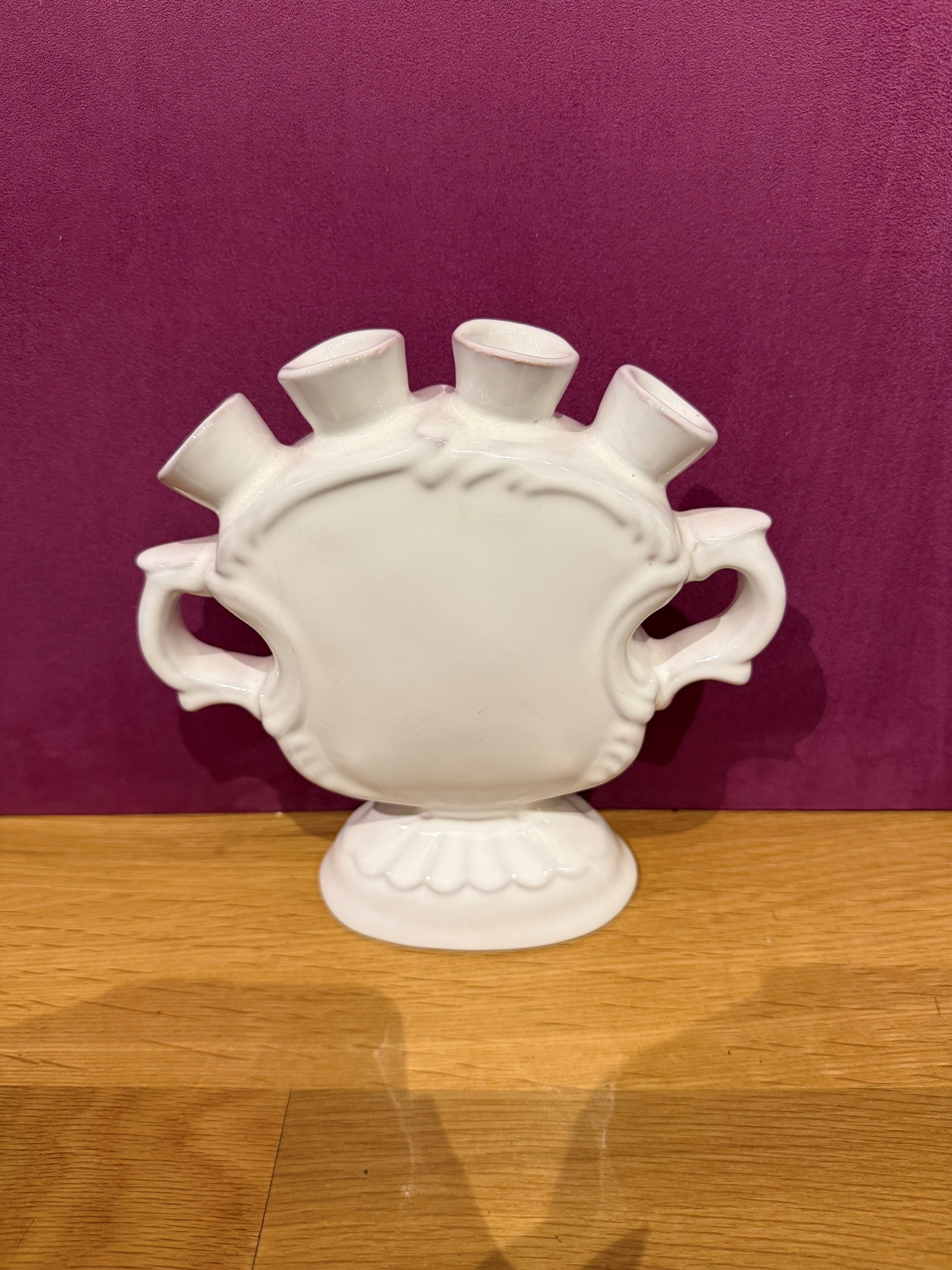 Weiße Tulpenvase mit mehreren Öffnungen, kunstvolles Design, auf einer Holzoberfläche mit violettem Hintergrund.