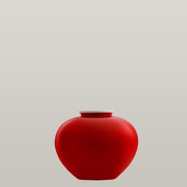 Rote, herzförmige Vase mit weißem Rand vor grauem Hintergrund.