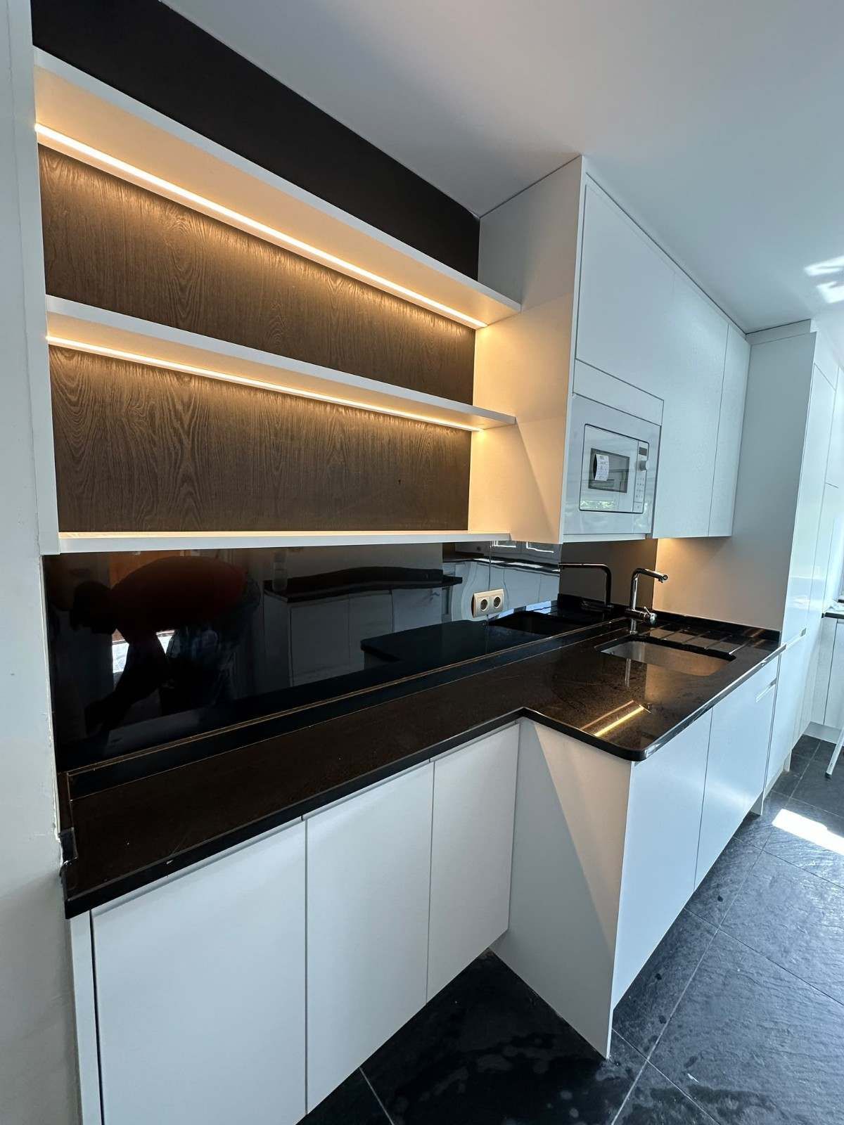 Cocina moderna con armarios blancos, encimeras negras, iluminación bajo los armarios y microondas empotrado