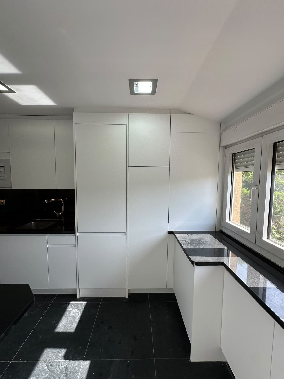 Cocina moderna y luminosa, con armarios blancos, encimera negra y ventanales