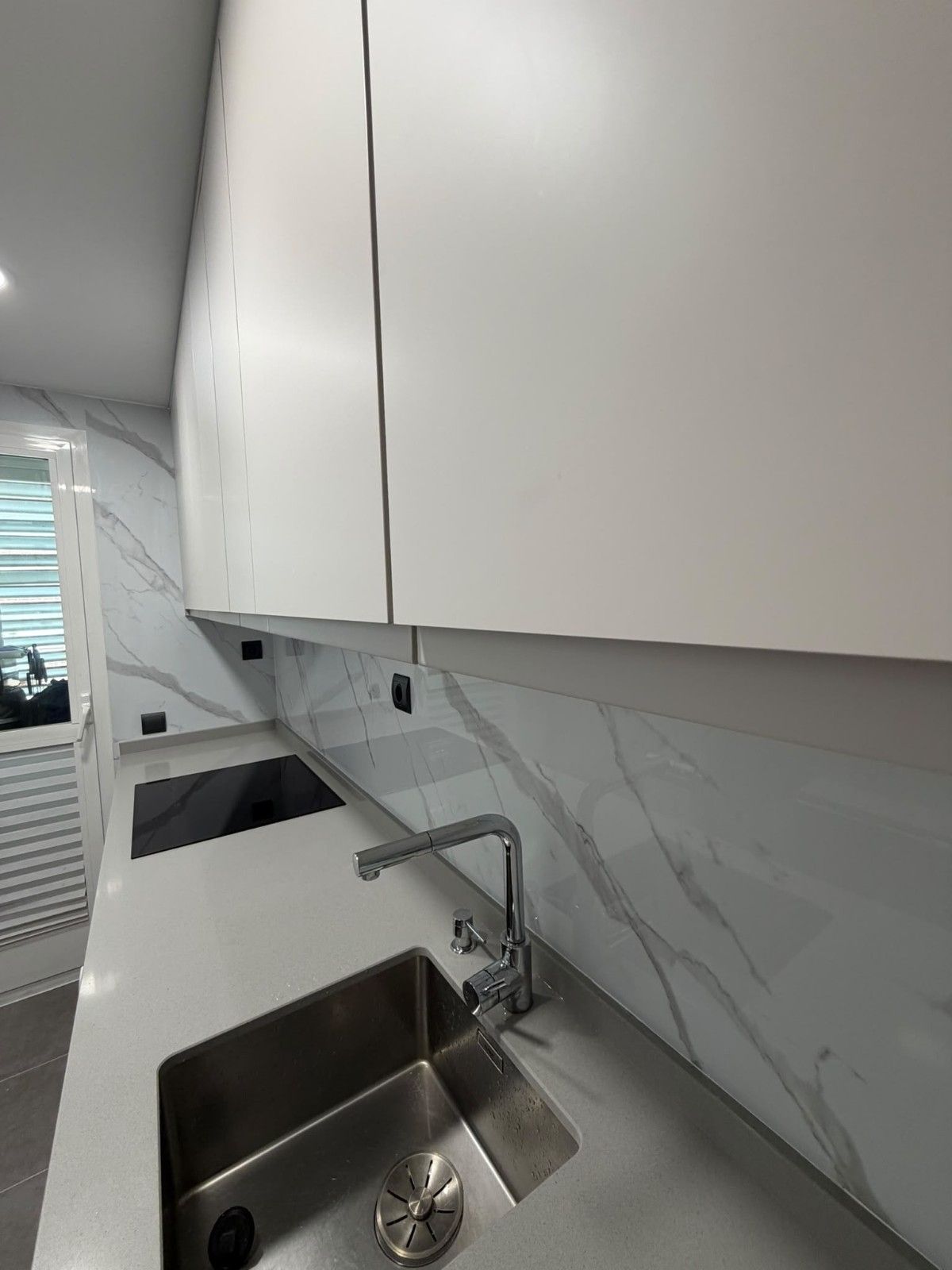 Cocina moderna con armarios blancos, salpicadero de mármol, fregadero de acero inoxidable y encimera negra con placa de cocina.