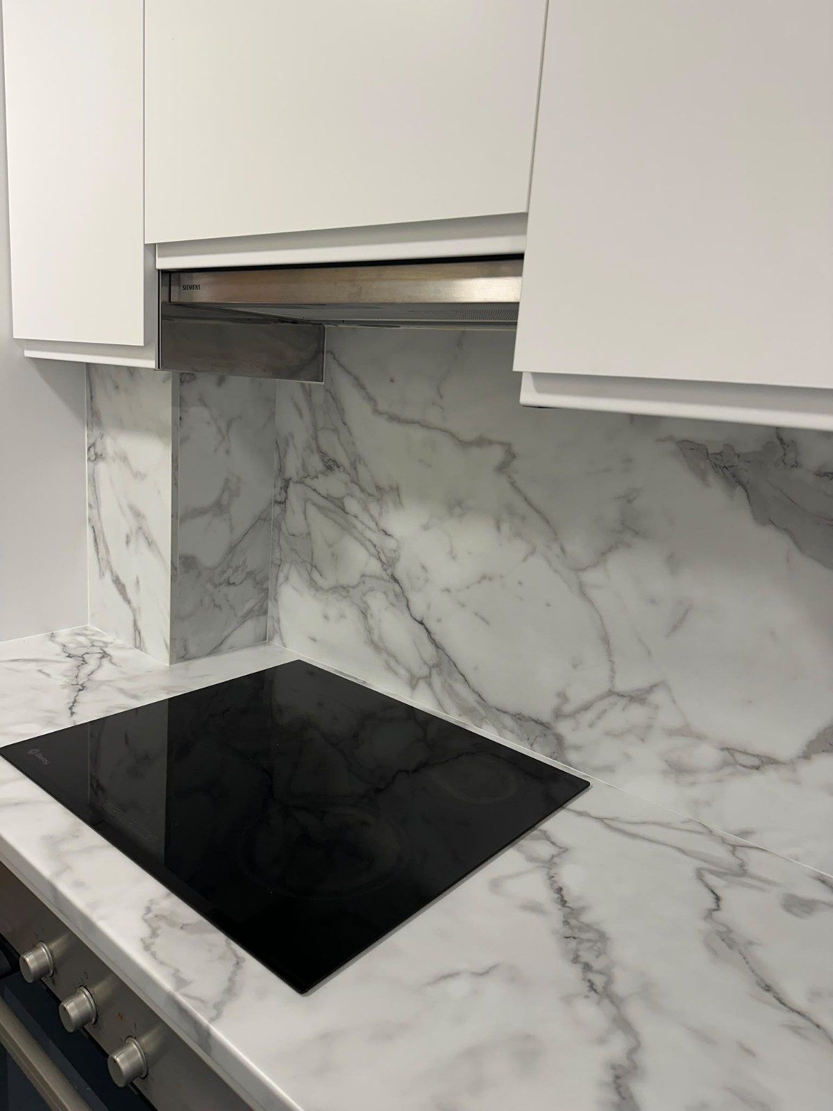 Cocina moderna con armarios blancos, salpicadero con diseño de mármol y placa de cocción de vitrocerámica negra