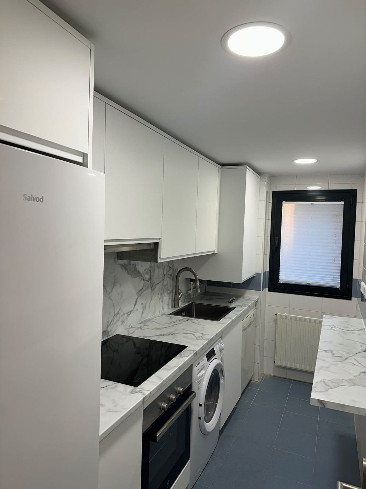 Cocina moderna blanca en paralelo, con encimera negra, lavadora y una ventana al fondo