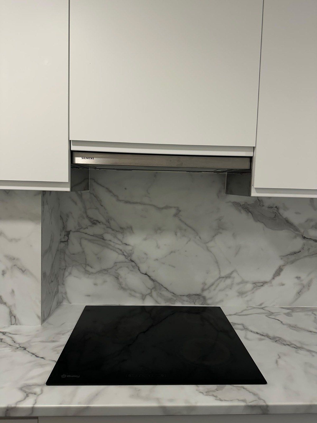 Cocina moderna con salpicadero de mármol, armarios blancos y placa de inducción negra