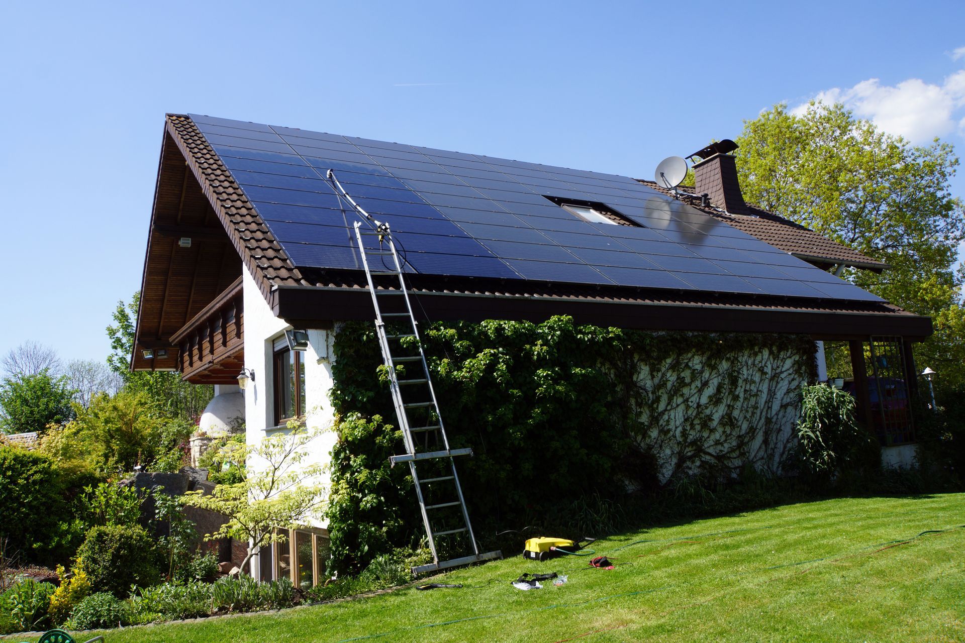 Maison avec des panneaux solaires sombres sur le toit, une échelle appuyée contre celui-ci pour le nettoyage.