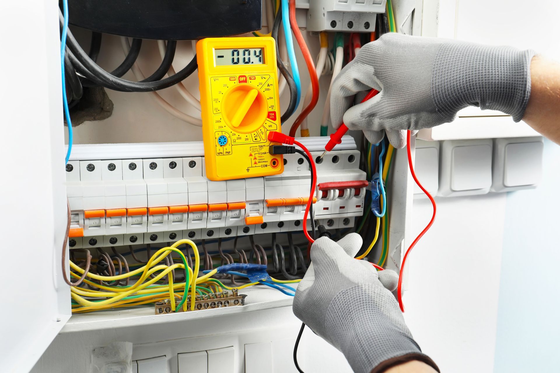 Un électricien teste un tableau électrique avec un multimètre jaune.