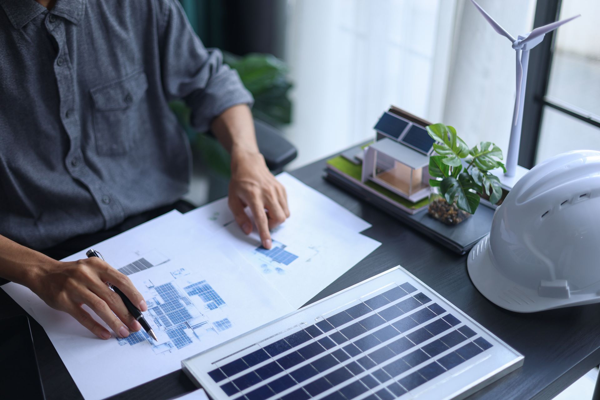 Une personne examine des plans de panneaux solaires à côté d'une maquette de maison.