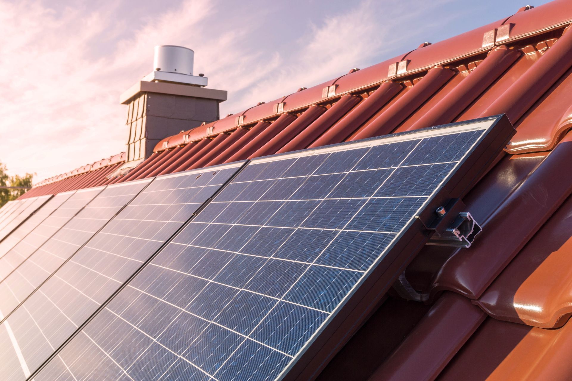 Des panneaux solaires installés sur un toit de tuiles rouges au coucher du soleil.