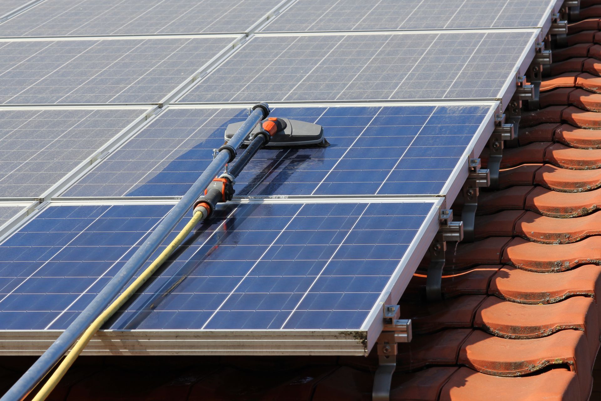 Nettoyage de panneaux solaires sur un toit en tuiles à l'aide d'un tuyau d'arrosage et d'une brosse.