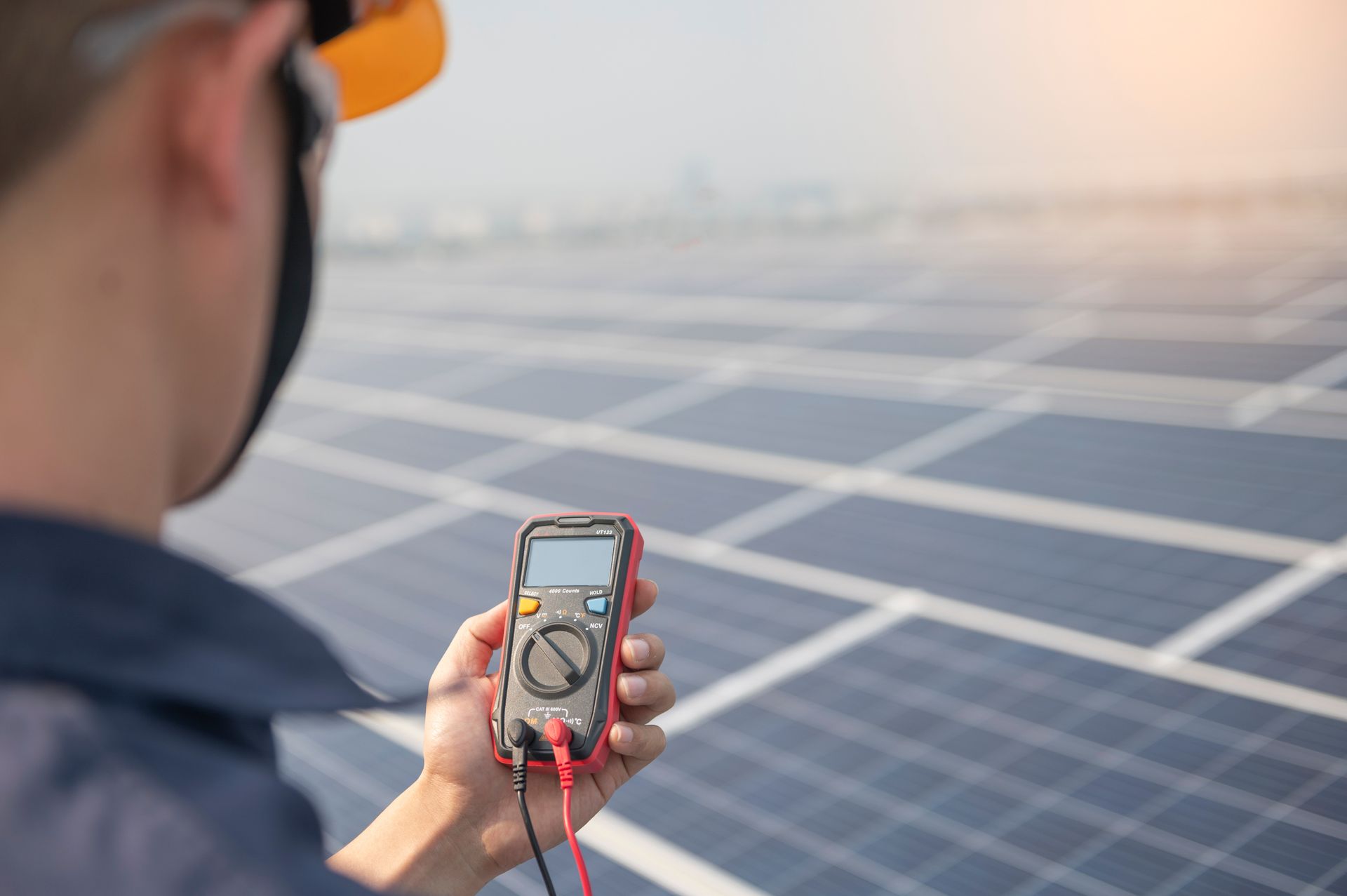 Une personne tient un multimètre près de panneaux solaires sur un toit.