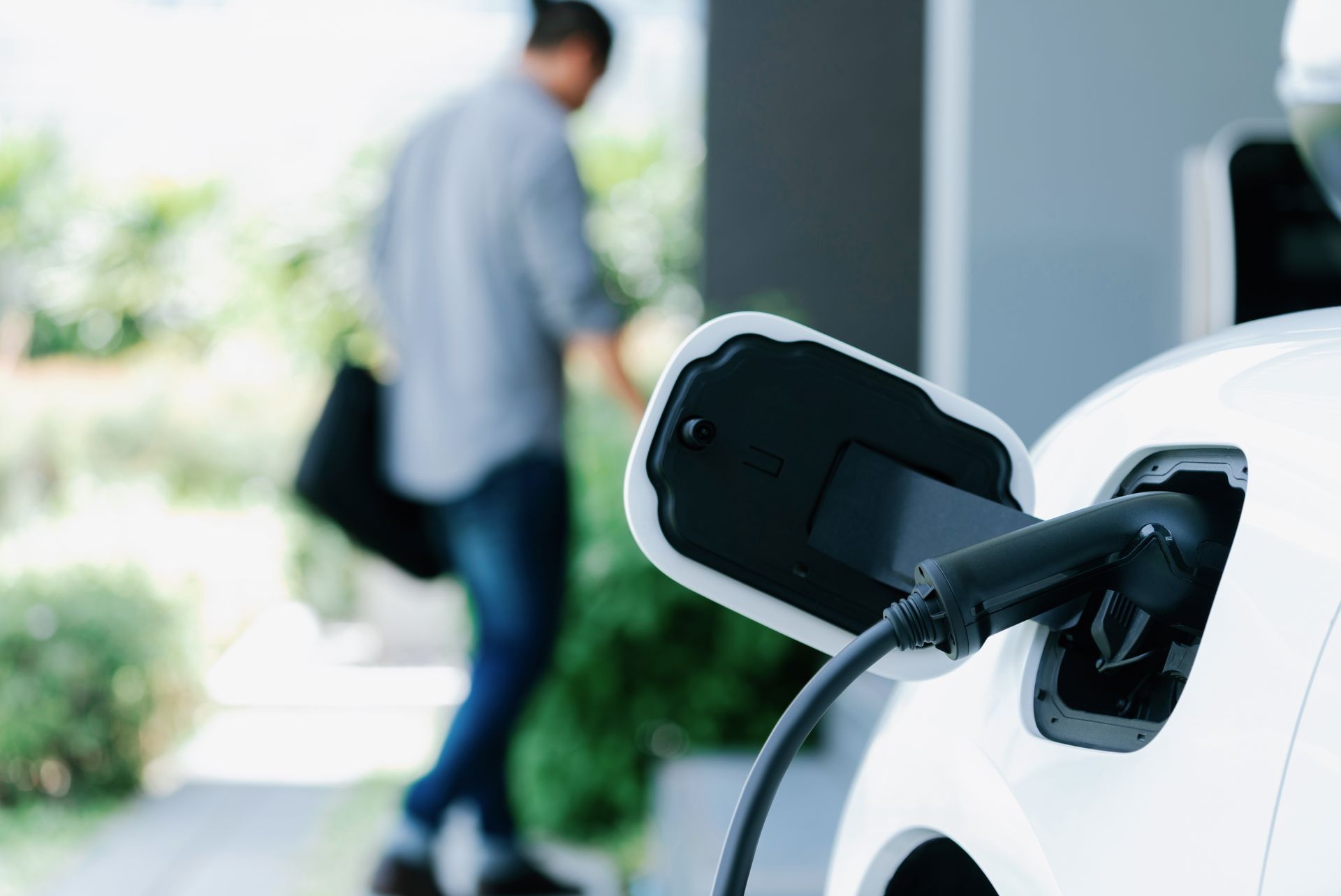 Recharge d'une voiture électrique dans une allée privée : une prise noire est connectée à un véhicule blanc.