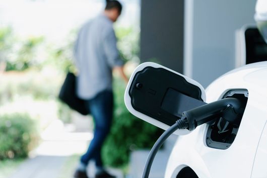 Recharge d'une voiture électrique dans une allée privée : une prise noire est connectée à un véhicule blanc.